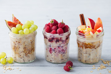 Assortment overnight oats, bircher muesli with fresh berries and fruits in a glass jars on wooden table background.