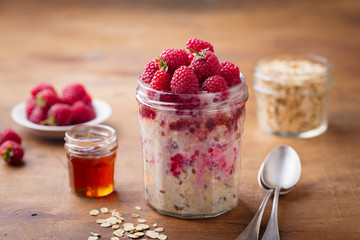 Overnight oats, bircher muesli with raspberry in a glass jar on wooden table background.