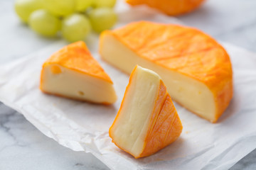 Cheese with washed orange rind. French or German. Marble table background. Close up.