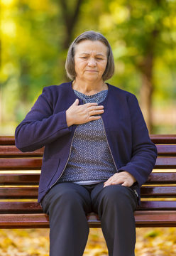 Puzzled aging woman having heart attack.  Senior lady clutching her chest in pain at the first signs of angina or a myocardial infarct or heart attack, upper body in park on an autumn day.