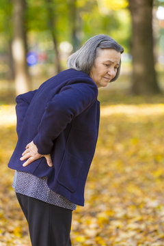 Senior woman suffering from backache outdoors in autumn park.