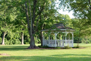 A white gazebo in the garden of the park on a summer day.