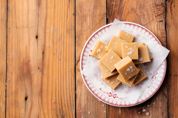 Fresh caramel fudge candies on a plate. Wooden background. Top view. Copy space.