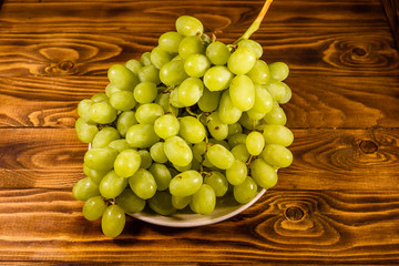 Ceramic plate with green grapes on wooden table