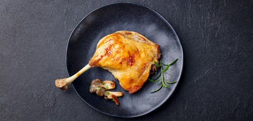 Duck leg confit with mushroom sauce on black plate. Slate background. Top view. © annapustynnikova