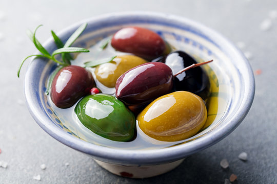 Olives assortment in bowl with oil. Stone background. Close up.