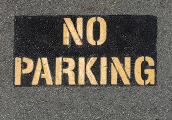 Yellow on black NO PARKING sign painted on parking lot asphalt.
