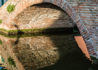 alte Brücke über einen Kanal in Comacchio, Italien, die sich im Wasser spiegelt