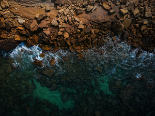 Aerial view of waves, rocks and transparent sea. Summer seascape. Top view from drone. Rocky coastline. 