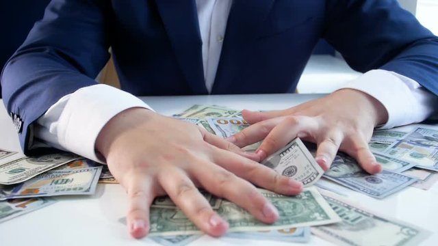 Slow motion video of greedy businessman grabing lots of money lying on office desk