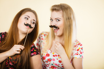 Two happy women holding fake moustache on stick