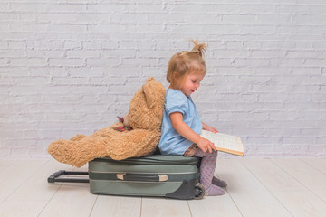 a girl, child on a background of white brick wall sitting on a suitcase with his back turned to the...