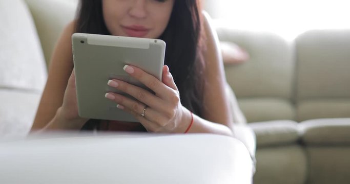 Woman using digital tablet PC app in home lying on sofa, focus on device