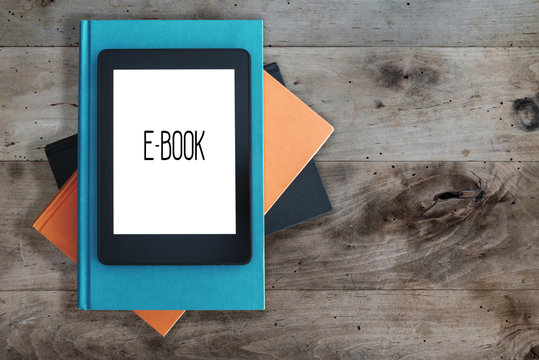 top view of e-book reader on a stack of books on rustic wooden table concept