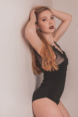 Fototapeta premium Boudoir photography of a beautiful woman standing near white wall in black body