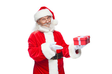 Christmas. Smiling Santa Claus in white gloves is holding a gift red box with a bow. Pointing at the gift. Isolated on white background.