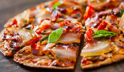 sliced Pizza with Mozzarella cheese, mushrooms, bacon, Tomatoes, pepper, Spices and Fresh Basil. Italian pizza on wooden background.