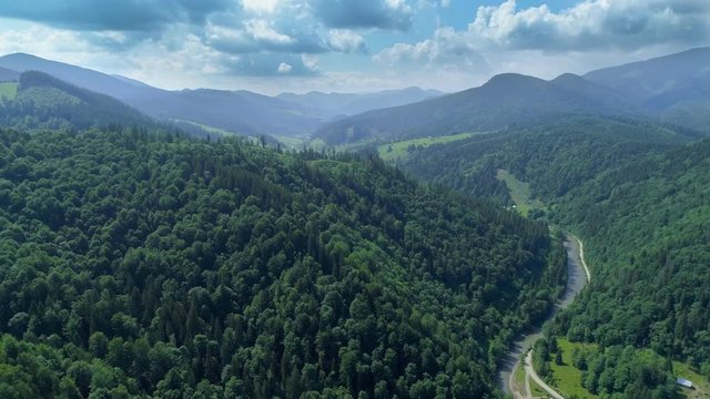 Hyperlapse flight over high mountains with a river snaking across countryside and a curly clouds background