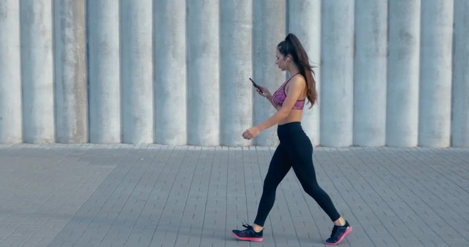 Full length shot of fit young woman choosing music before jogging outside. Fitness model exercising in morning outdoors. Healthy lifestyle concept. 4K