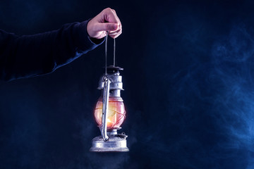 Man hand holding gas lantern on dark and night smoked foggy background. Gas or oil lamp burning. Horror and Halloween concept. Close up, selective focus. © Emilija