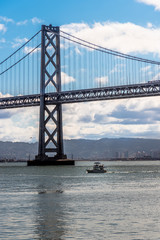 bay bridge and a boat in san francisco, view of the bay bridge in san francisco and a boat passing below it during morning.