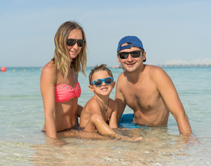 Happy family having fun on tropical white beach. Mother, father, a cute son. Positive human emotions, feelings, joy. Funny cute child making vacations and enjoying summer. Spring and summer holidays.
