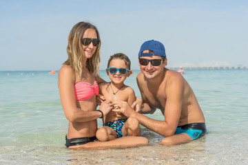 Happy family having fun on tropical white beach. Mother, father, a cute son. Positive human emotions, feelings, joy. Funny cute child making vacations and enjoying summer. Spring and summer holidays.