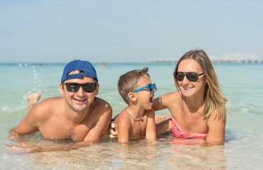 Obraz premium Happy family having fun on tropical white beach. Mother, father, a cute son. Positive human emotions, feelings, joy. Funny cute child making vacations and enjoying summer. Spring and summer holidays.
