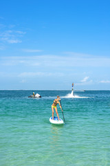 Young woman stand up on board and man posing at new flyboard at Caribbean tropical beach. Standup...