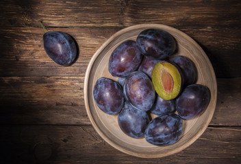 Ceramic bowl with plums over dark wooden board. Fruit background. Top view. Agriculture, Gardening, Harvest Concept.