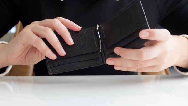 Slow motion video of young woman shaking empty wallet. One coin falling out of purse on table