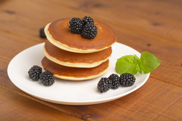 Delicious pancakes with BlackBerry and mint, on a white plate and a wooden table