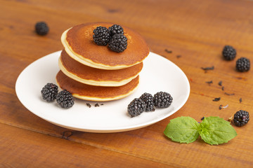 Delicious pancakes with BlackBerry and mint, on a white plate and a wooden table