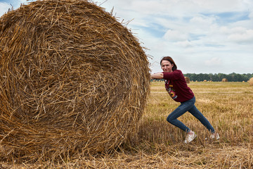 Naklejka na ściany i meble young girl having fun in the field, pushes the haystack