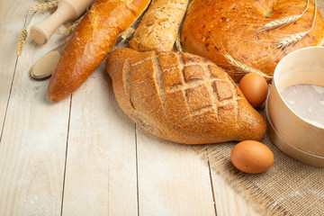 Fresh bread on a wooden table with flour and wheat, eggs and empty space. Concept baking, bakery