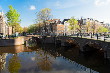 Obraz premium historical houses and arches of bridge over canal with mirror reflections, Amsterdam, Netherlands