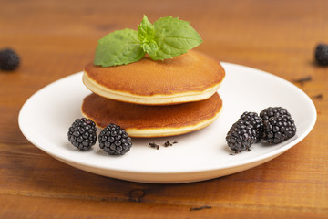 Delicious pancakes with BlackBerry and mint, on a white plate and a wooden table