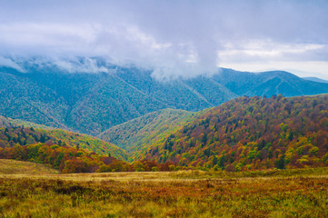 Fototapeta na wymiar Autumn colors in the background of remote mountains. Clouds fly between the mountains. Autumn mountain landscape