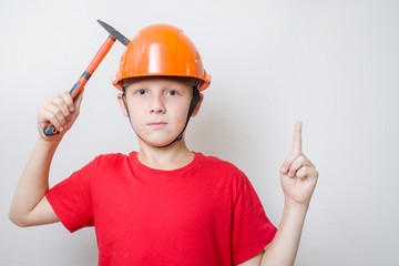 Boy in helmet, hard hat with idea gesture. Young builder with hocked face knocks with hammer on...