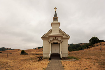 Fototapeta na wymiar Small white church on dry brown grass in rural California