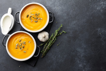 Pumpkin soup with thyme herb, cream and pumpkin seeds served in two black bowls, top view