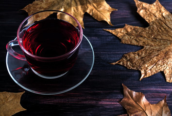 Cup of tea with autumn leaves on a black wooden background.