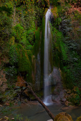 Fototapeta premium Blurred waterfall comes from inside the red rocks with Green trees and plants around
