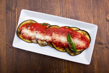 Eggplant parmigiana on a wooden table seen from above