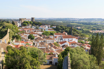 Fototapeta na wymiar Scenic view of white houses red tiled roofs, and castle from wall of fortress. Beautiful old town with medieval. Obidos village, Portugal. Summer sunny day.