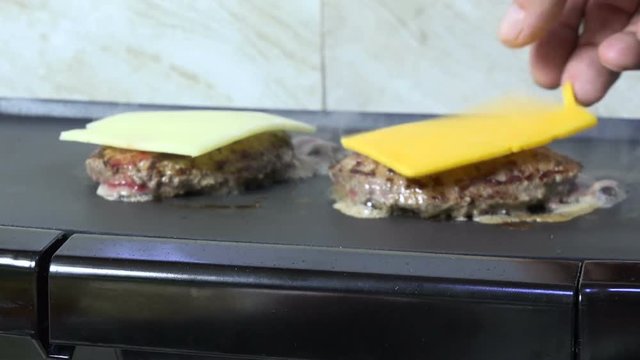 Adding cheddar and swiss cheese slices to burgers on a grill
