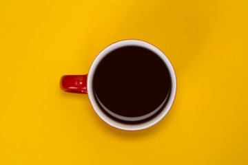 Red cup with coffee on a yellow background. View from above.