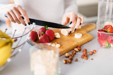 Fresh banana and strawberries are being cut by a young female on a wooden cutting board.
