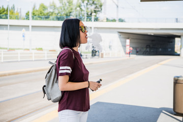 Stylish girl smoking an e-cigarette as she is walking through the city.