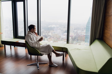 Carefree guy relaxing with hot drink at luxury apartments with great city view